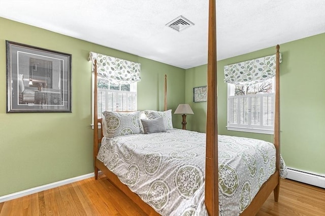 bedroom with baseboard heating, baseboards, visible vents, and wood finished floors