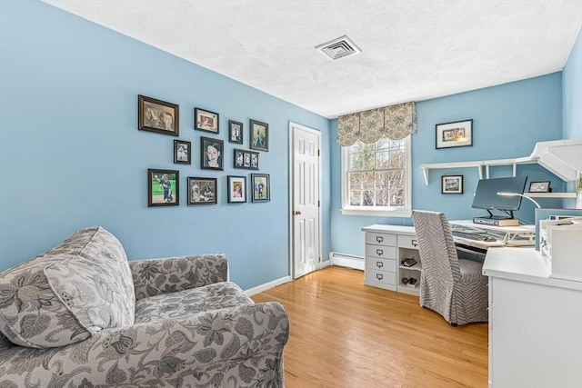 office with baseboard heating, a textured ceiling, baseboards, light wood-type flooring, and visible vents