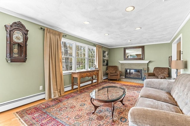 living area with a brick fireplace, a textured ceiling, ornamental molding, and wood finished floors