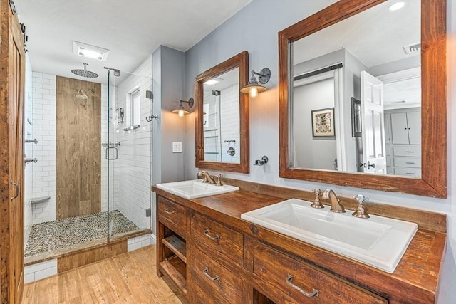 full bath featuring double vanity, a shower stall, a sink, and wood finished floors