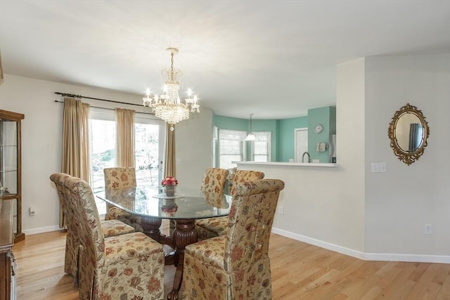 dining area with light wood-style flooring, a healthy amount of sunlight, baseboards, and a notable chandelier