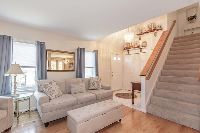 living room with a notable chandelier, light wood-style flooring, stairs, and a healthy amount of sunlight