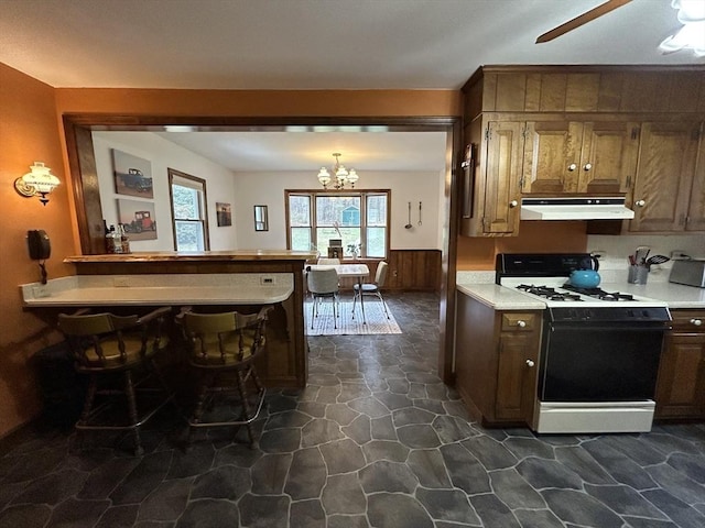 kitchen with range with gas stovetop, wainscoting, stone flooring, light countertops, and under cabinet range hood