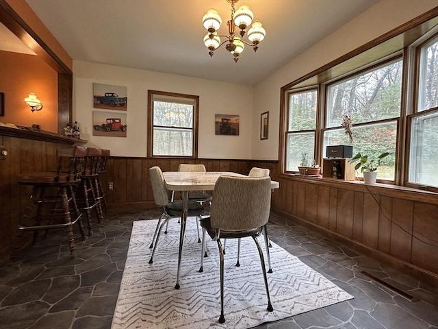 dining room featuring stone flooring, built in features, wood walls, a wainscoted wall, and a notable chandelier