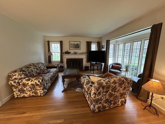 living area featuring wood-type flooring, baseboards, and a brick fireplace