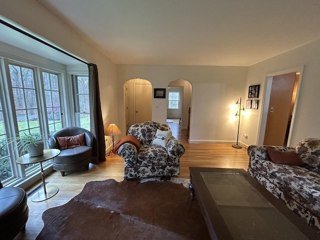 living area with arched walkways, baseboards, plenty of natural light, and wood finished floors
