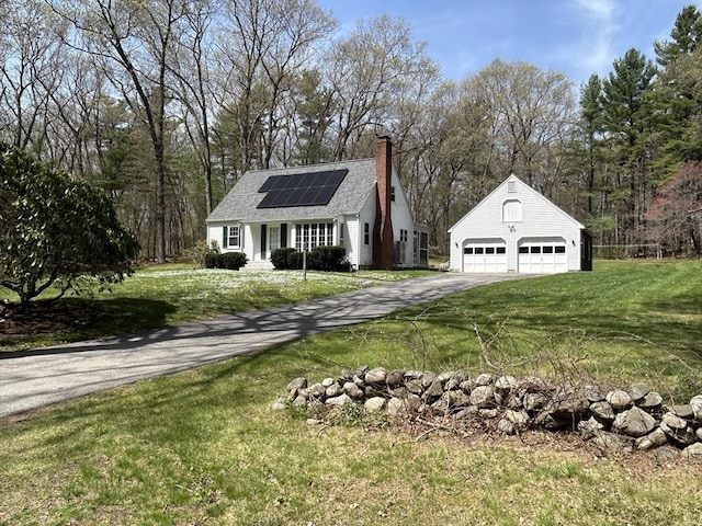 view of front of property with roof mounted solar panels, a chimney, an outdoor structure, and a front lawn