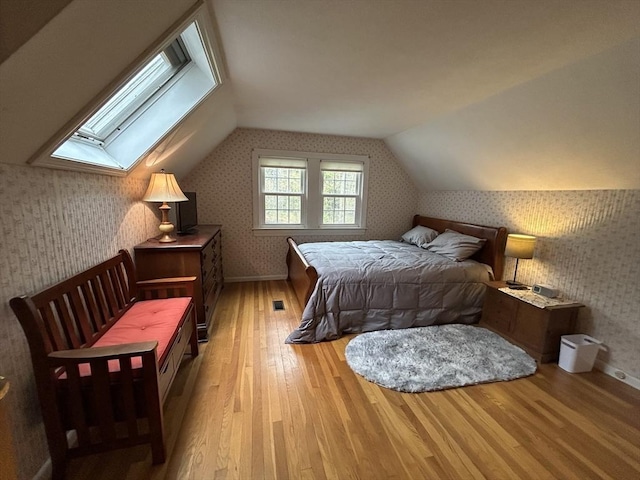 bedroom with baseboards, wallpapered walls, hardwood / wood-style floors, and lofted ceiling with skylight