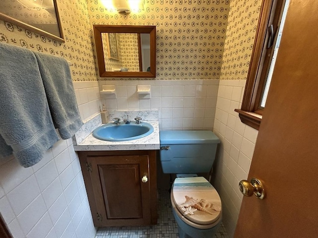 bathroom featuring toilet, wallpapered walls, tile walls, and wainscoting