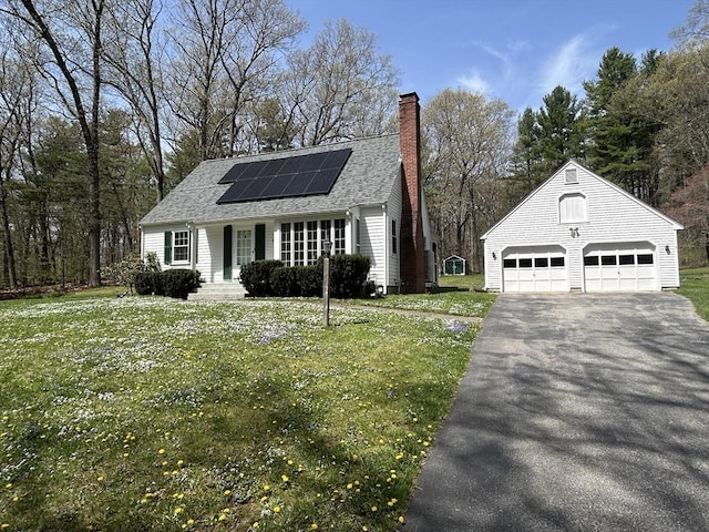 view of front facade with aphalt driveway, a front yard, roof mounted solar panels, an outbuilding, and a chimney