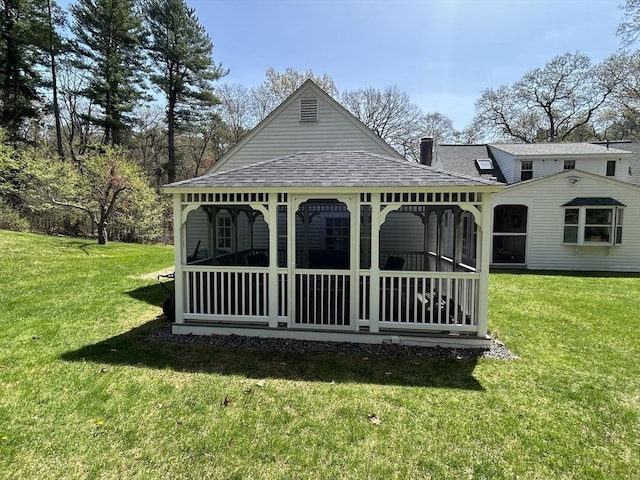 exterior space with a sunroom, a shingled roof, a lawn, and a chimney