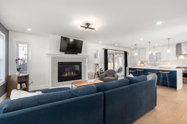 living area with a healthy amount of sunlight, recessed lighting, light wood-style floors, and a tile fireplace