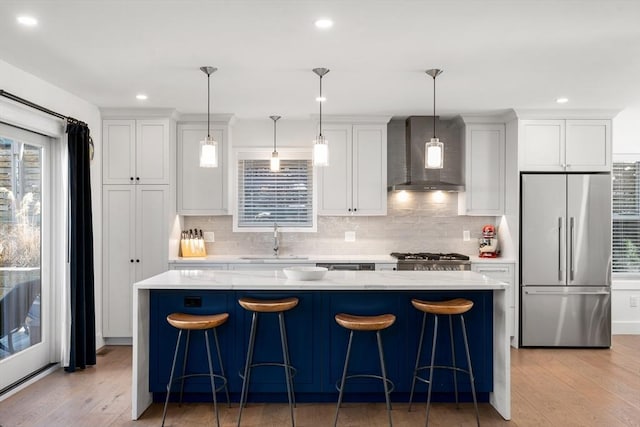 kitchen with a sink, a kitchen island, light wood-style floors, high quality fridge, and wall chimney range hood