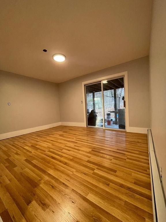 empty room featuring a baseboard heating unit, baseboards, and light wood finished floors