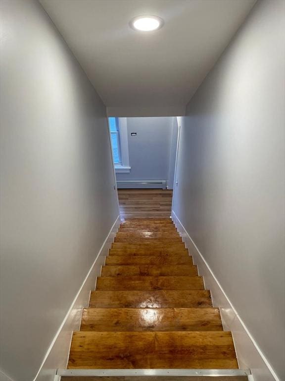 stairway with a baseboard heating unit, baseboards, and wood finished floors