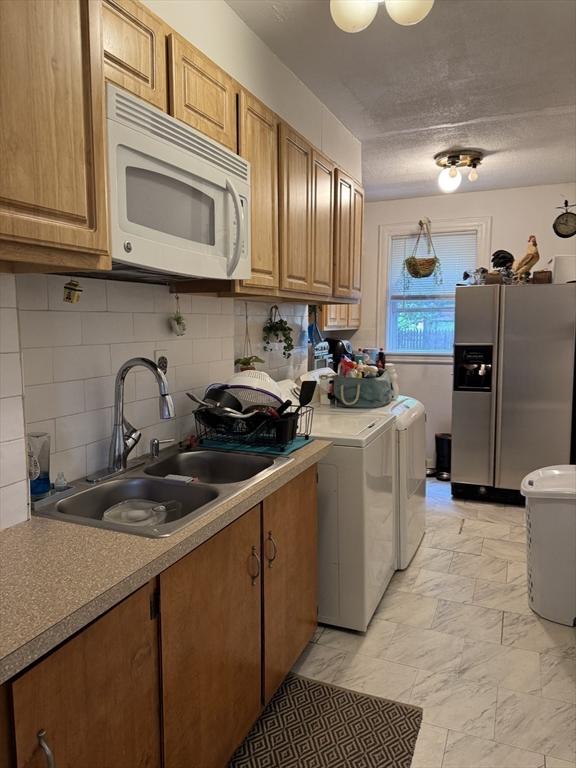 348 Fairmount St, Fitchburg, MA 01420 - kitchen with white microwave, stainless steel fridge with ice dispenser, a sink, washer and clothes dryer, and backsplash