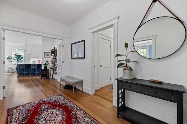 hallway with light wood finished floors, ornamental molding, and baseboards