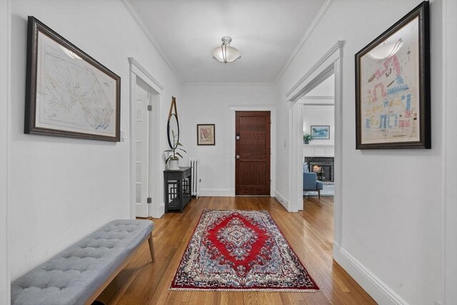 foyer entrance featuring wood finished floors, a lit fireplace, ornamental molding, and baseboards
