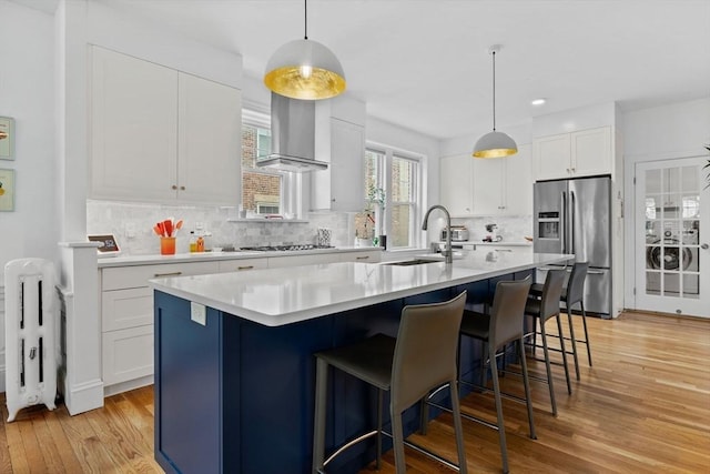 kitchen with stainless steel fridge, a sink, wall chimney range hood, light wood finished floors, and white gas cooktop