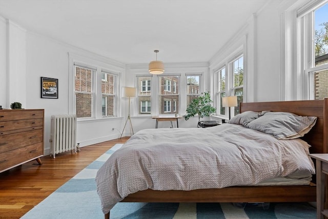 bedroom with radiator, wood finished floors, multiple windows, crown molding, and baseboards