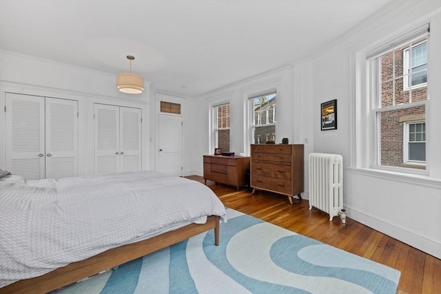 bedroom featuring radiator heating unit, hardwood / wood-style floors, multiple closets, baseboards, and crown molding