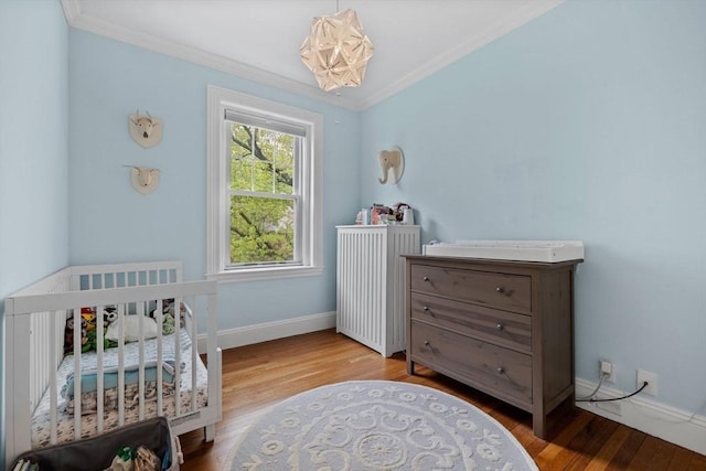 bedroom with crown molding, wood finished floors, a chandelier, baseboards, and a nursery area