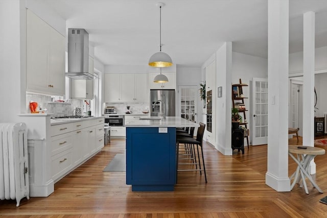 kitchen featuring wall chimney range hood, radiator heating unit, backsplash, light countertops, and white cabinets