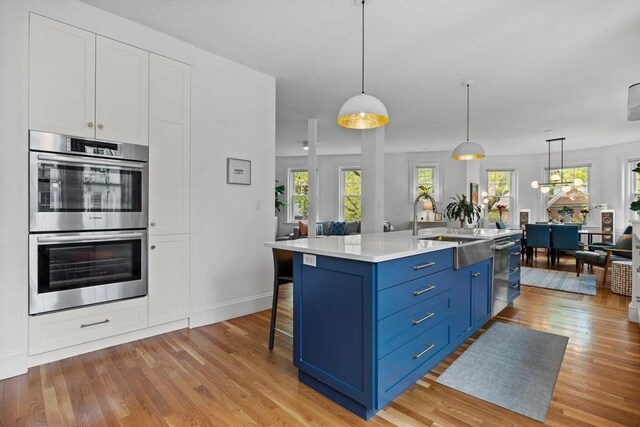 kitchen with blue cabinets, a sink, appliances with stainless steel finishes, and light wood-type flooring