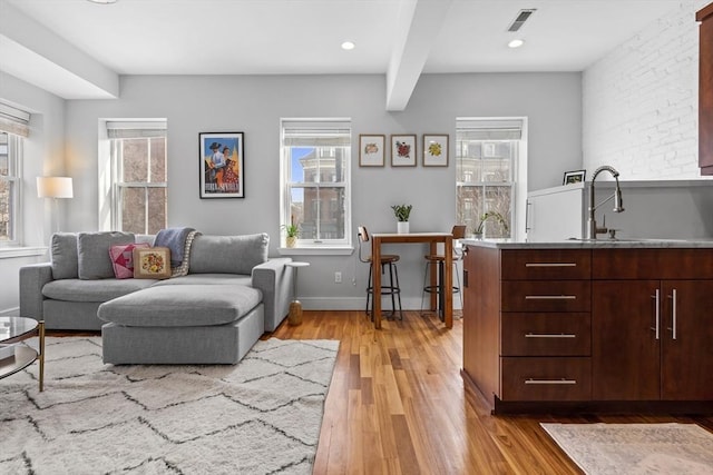 living area with light wood-type flooring, a wealth of natural light, beam ceiling, and visible vents