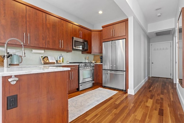 kitchen featuring wood finished floors, visible vents, high quality appliances, light countertops, and decorative backsplash