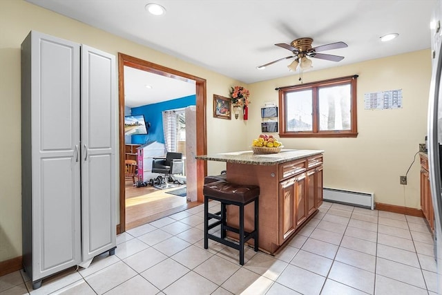 kitchen featuring light tile patterned flooring, a kitchen bar, a baseboard radiator, a kitchen island, and ceiling fan