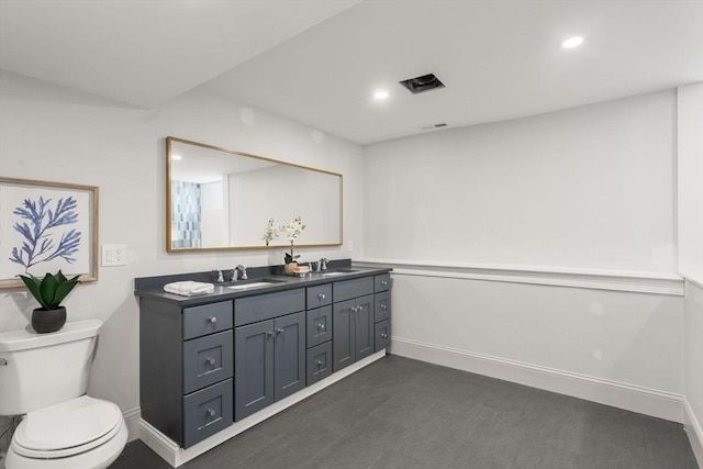 bathroom with double vanity, a sink, toilet, and baseboards