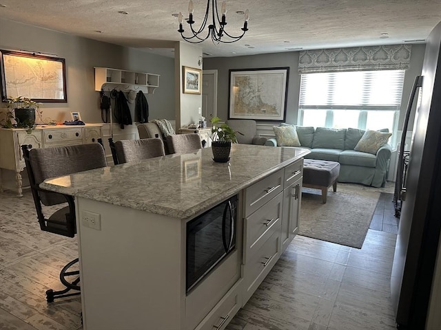 158 Quincy Shore Dr Unit 78, Quincy, MA 02171 - kitchen featuring open floor plan, a kitchen bar, black microwave, a textured ceiling, and a chandelier