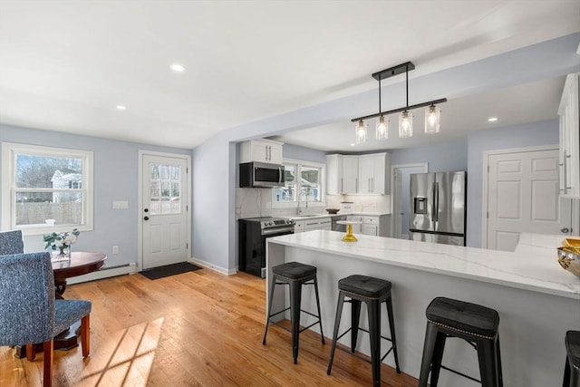 kitchen with stainless steel appliances, white cabinetry, a kitchen bar, kitchen peninsula, and a baseboard radiator