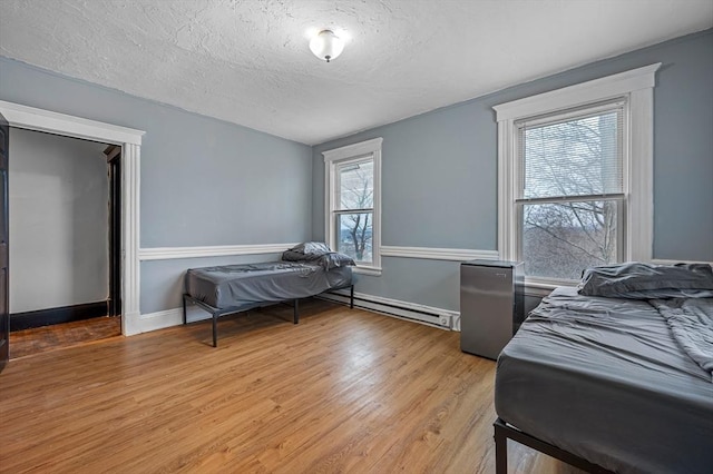 bedroom with baseboard heating, light wood-type flooring, a textured ceiling, and baseboards