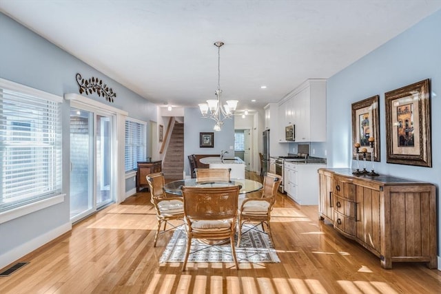 dining room with a notable chandelier, visible vents, light wood-type flooring, baseboards, and stairs