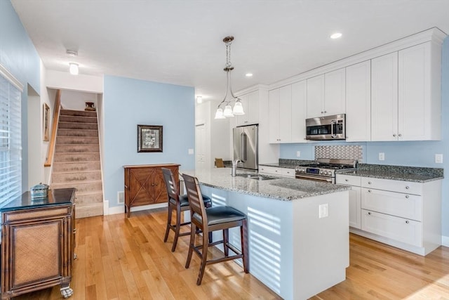 kitchen featuring light wood-type flooring, white cabinets, stainless steel appliances, and a sink