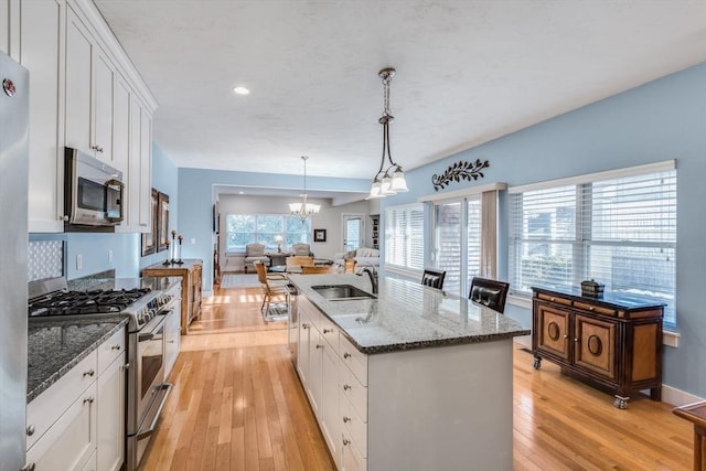 kitchen with appliances with stainless steel finishes, light wood-style floors, white cabinetry, a sink, and a chandelier