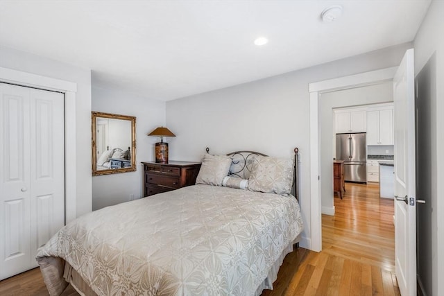 bedroom with a closet, light wood-type flooring, freestanding refrigerator, and baseboards