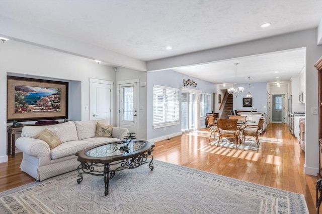 living area featuring a chandelier, stairway, light wood-style flooring, and baseboards