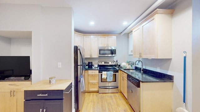 kitchen with dark stone countertops, recessed lighting, a sink, stainless steel appliances, and light wood-style floors