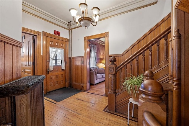 entrance foyer featuring a chandelier, light wood-style flooring, stairs, wainscoting, and crown molding