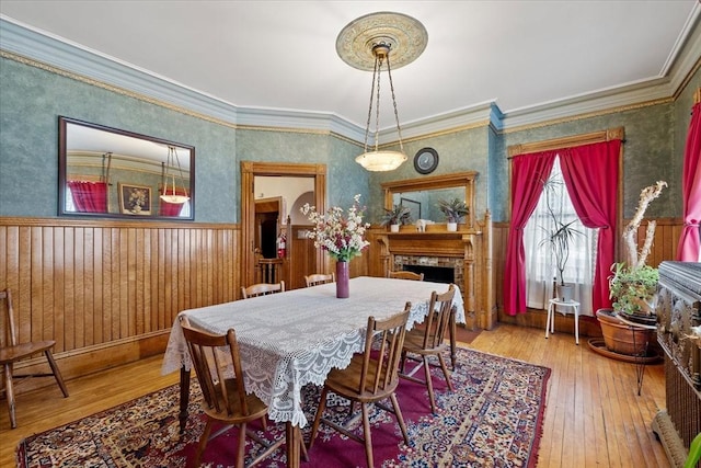 dining area featuring hardwood / wood-style flooring, a fireplace, baseboards, wainscoting, and crown molding