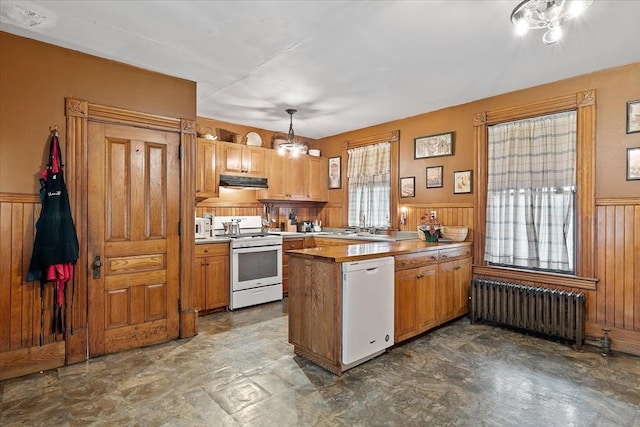 kitchen with white appliances, wainscoting, radiator, a peninsula, and under cabinet range hood