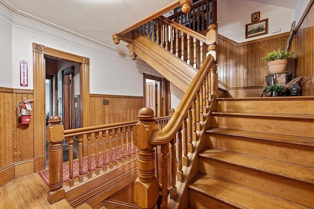 stairway featuring wood walls, ornamental molding, wood finished floors, and wainscoting