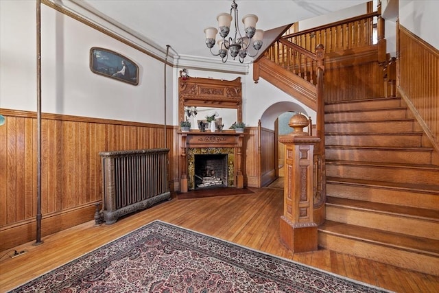 living room featuring a notable chandelier, a wainscoted wall, wood walls, wood finished floors, and stairway