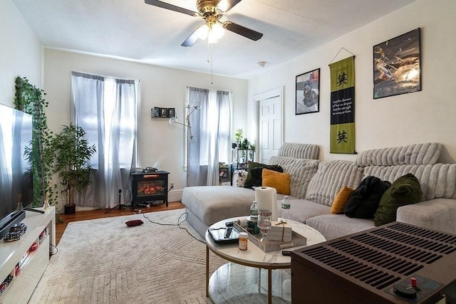 living area featuring a wood stove, wood finished floors, and ceiling fan