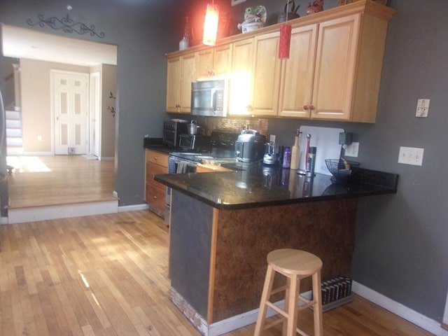 14 Mutton Ln, Weymouth, MA 02189 - kitchen featuring light brown cabinetry, light wood-style floors, dark countertops, and a breakfast bar