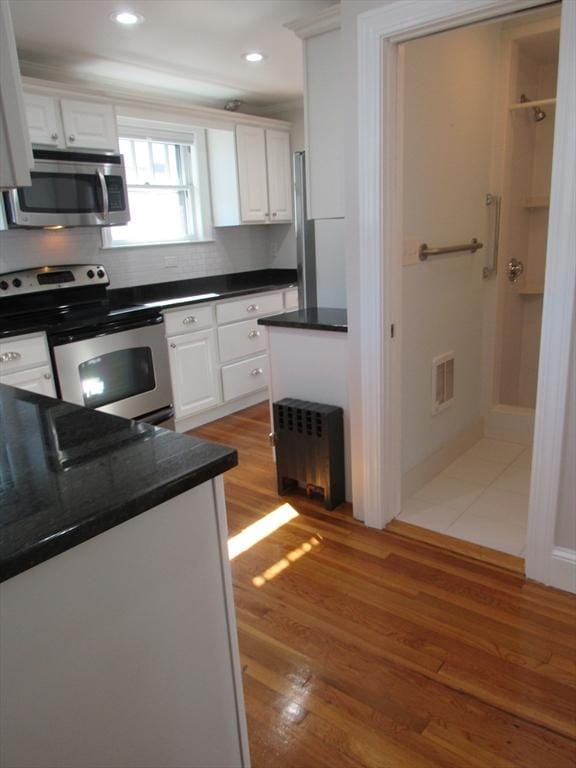 kitchen with dark countertops, tasteful backsplash, light wood finished floors, stainless steel appliances, and white cabinetry