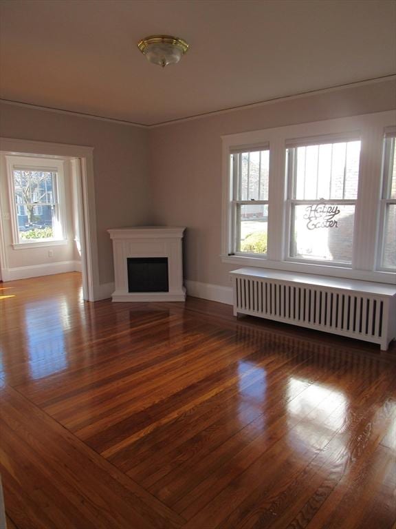 unfurnished living room featuring radiator, baseboards, a fireplace, and wood finished floors